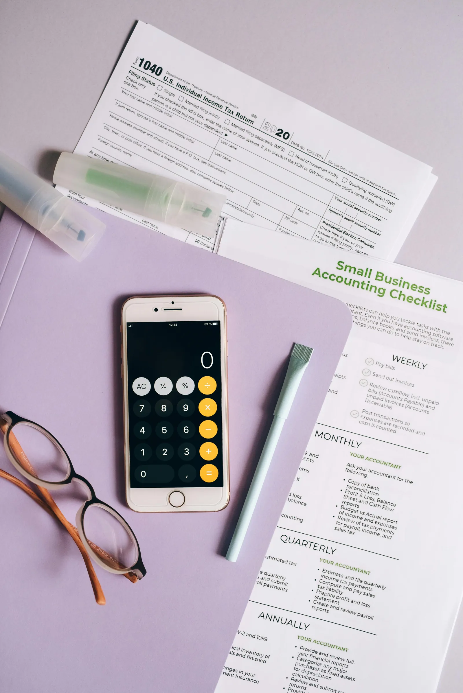 Calculator phone beside small-business accounting checklist papers.